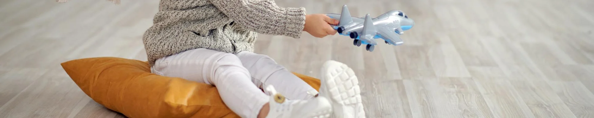 child sitting on an orange pillow playing with a silver and blue airplane